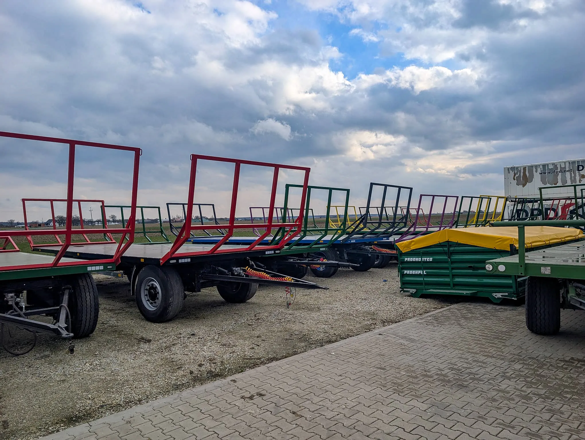 Przyczepy platformowe ERMAR w różnych kolorach ustawione na placu